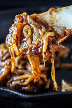 a spoon full of food is being lifted from a skillet with meat and cheese on it