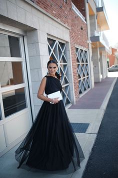 a woman in a long black dress standing on the side of a building with her hands in her pockets