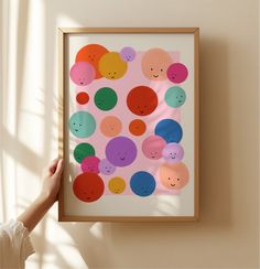 a person holding up a framed art piece with colorful circles and smiley faces on it