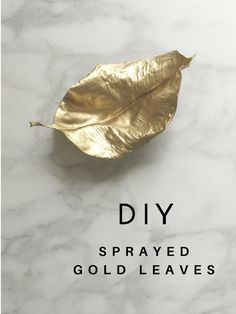 a gold leaf sitting on top of a white marble surface with the words diy sprayed gold leaves