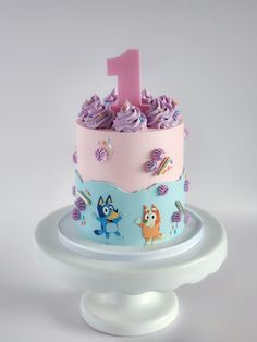 a pink and blue birthday cake with cartoon characters on the frosting is sitting on a white pedestal