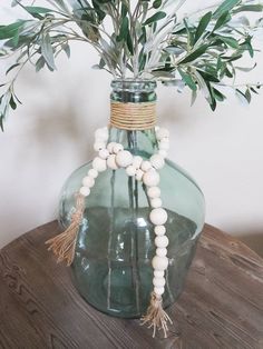 a green vase with white beads and greenery in it sitting on a wooden table