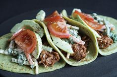 three tortillas topped with meat, cheese and tomatoes on top of a black plate