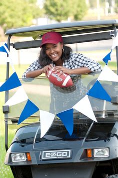 a woman is holding a football in her hand and posing for the camera while sitting on a golf cart