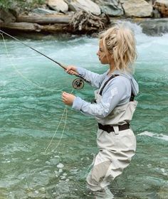 a woman standing in the water while holding a fishing rod