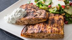 a white plate topped with meat patties, salad and cucumber on top of it