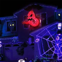 a house covered in christmas lights with a large red ghost on it's roof