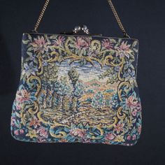 A ladies handbag with gold coloured metal clasp with dots. Vintage handmade. Fine example of a cosy lady's handbag of the beginning of the last century. Embroidered fabric with a landscape surrounded by flowers on both sides of the bag. Ivory coloured satin inside. Lovingly made. Vintage. Size  W 16 H 16 cm. It has been around for a long time but just a tiny bit of wear. Still beautiful and surely wearable on your next garden party. Please have a look at all our vintage handbags in the  - Ladies Vintage Tapestry Pouch Bag, Vintage Handmade Tapestry Bag, Vintage Tapestry Handmade Bags, Antique Tapestry Bags For Everyday, Vintage Embroidered Tapestry Shoulder Bag, Vintage Embroidered Rectangular Evening Bag, Victorian Style Rectangular Tapestry Bag, Victorian Style Embroidered Rectangular Bag, Antique Handmade Rectangular Shoulder Bag