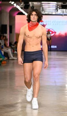 a man with no shirt on walking down the runway wearing shorts and bandannas