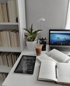 an open book sitting on top of a white desk next to a laptop computer and cup of coffee