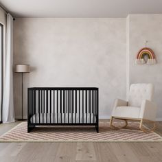 a baby's room with a rocking chair, crib and rainbow wall hanging