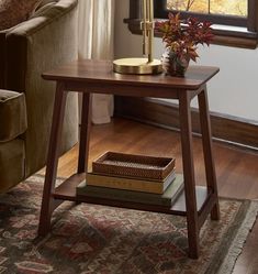 a table with books and a lamp on it in front of a window next to a couch