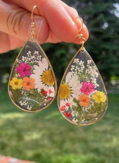 a pair of earrings that have flowers painted on the inside of them, hanging from gold earwires