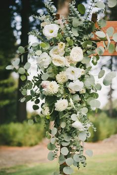 an arrangement of flowers and greenery hanging from a wooden cross