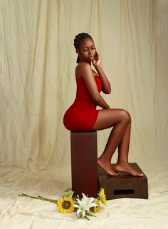 a woman in a red dress sitting on top of a wooden box next to sunflowers