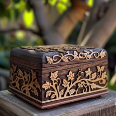 an ornate wooden box sitting on top of a piece of wood in front of a tree