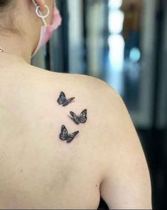 the back of a woman's shoulder with three butterflies on her left arm and behind her ear