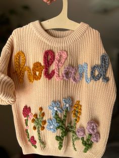 a hand knit sweater with flowers and the word love spelled in multicolored letters