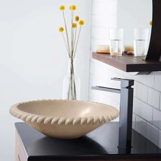 a bowl shaped sink sitting on top of a counter next to a vase with yellow flowers