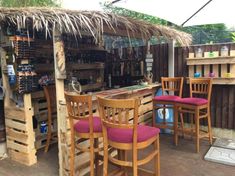 several wooden chairs and tables in front of a bar with tiki hut style roof