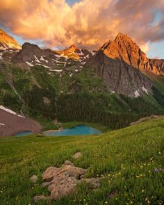 the mountains are covered in green grass and wildflowers as the sun is setting