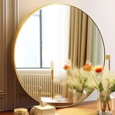 a round mirror sitting on top of a table next to a vase filled with flowers