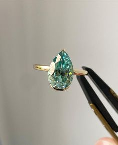 a ring with an aqua colored diamond on it next to some black pens and scissors