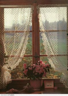 an old fashioned window with lace curtains and pink flowers in the vase on the windowsill