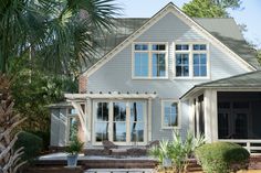 a large gray house with lots of windows on the front and side of it, surrounded by palm trees