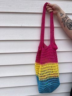 a person holding up a crocheted bag hanging on the side of a house