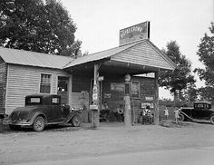 black and white photograph of an old gas station with cars parked in front of it