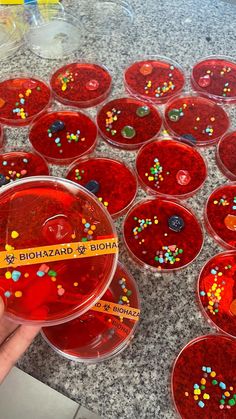 a person holding up a red substance in front of many bowls with colorful sprinkles on them