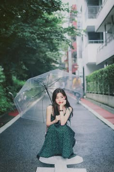 a woman is sitting on the street with an umbrella in her hand and she is wearing a green polka dot dress