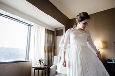 a woman in a white dress is standing near a window