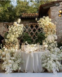 a table with white flowers and candles on it in front of a brick wall at a wedding