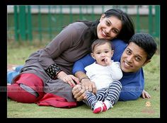 a man, woman and baby are laying on the ground in front of a green fence