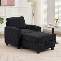 a black chair and ottoman in a room with white walls, rugs and windows