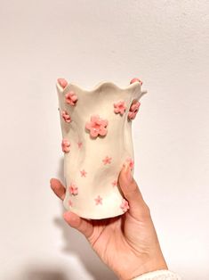 a hand holding a white vase with pink flowers on it