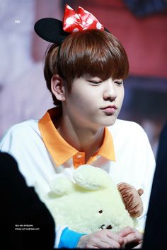 a young man holding a teddy bear wearing a red bow on top of his head