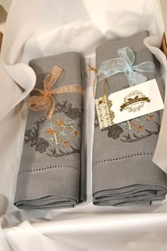 two folded gray napkins in a box with ribbon and tags on the top one