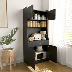 an open cabinet in the corner of a room next to a potted plant and window