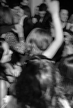 black and white photograph of people dancing at a party with their arms in the air