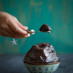 a person holding a spoon over a bowl with chocolate souffle on it and sprinkled with powdered sugar