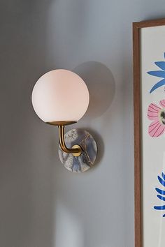 a wall light mounted on the side of a wall next to a framed art piece