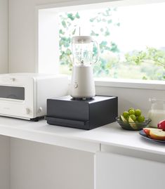 a white blender sitting on top of a counter next to a bowl of fruit