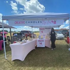 a woman standing next to a table under a white tent with pink writing on it