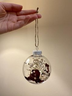 a hand is holding a glass ornament with flowers in it on a string