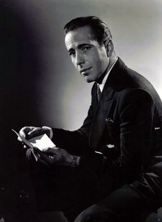 a man in a suit and tie sitting on a chair holding a book while looking at the camera