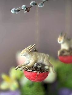 two small ornaments hanging from strings with animals on them and flowers in the back ground