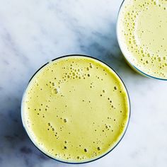 two glasses filled with yellow liquid sitting on top of a white countertop next to each other